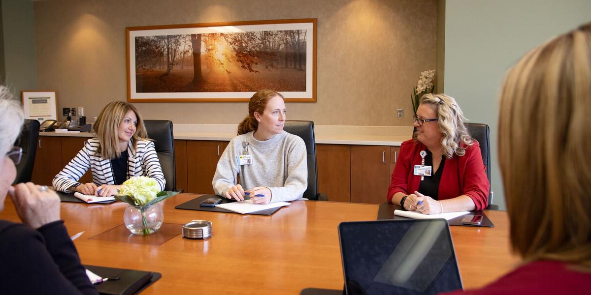 Five women sitting in a conference room having a meeting.